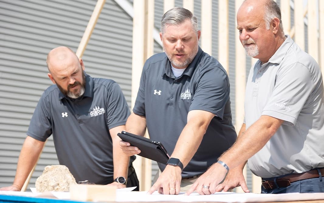 Three contractors looking at home floorplans on a residential construction site.