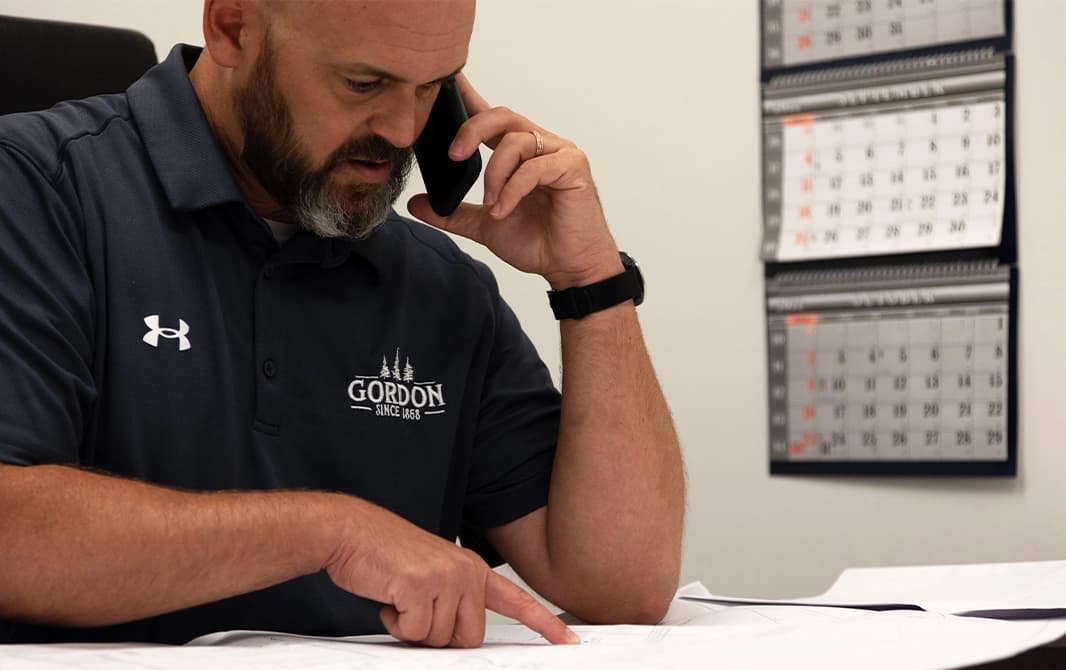 Man talking with client and referencing details from a blueprint that is on his desk.