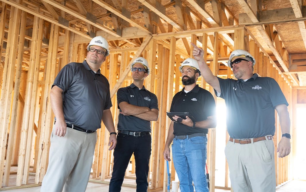 Four employees standing in a home building site and discussing building plans.