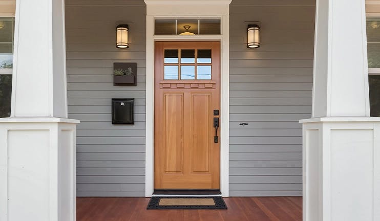 Wood front door on a grey house with a white trimmed front porch.